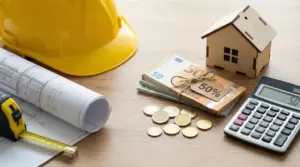 Casco giallo, progetto edilizio, soldi, calcolatrice e modellino di casa su un tavolo