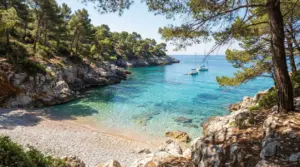 Cala nascosta con acqua turchese e barche a vela ormeggiate, circondata da pini e rocce